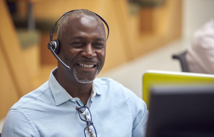 Portrait Of Mature Businessman Wearing Phone Headset Talking To Caller In Customer Services Centre