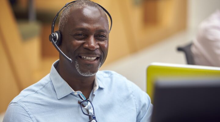 Portrait Of Mature Businessman Wearing Phone Headset Talking To Caller In Customer Services Centre